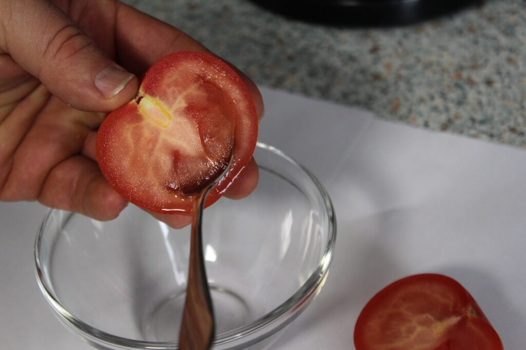 Das Foto zeigt, wie die Samen einer Tomate entfernt werden